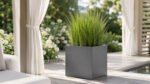 Grauer, quadratischer Pflanzkübel Alessio 2 aus Aluminium mit üppigem grünem Ziergras in einer hellen, modernen Gartenpergola