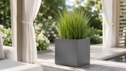Grauer, quadratischer Pflanzkübel Alessio 2 aus Aluminium mit üppigem grünem Ziergras in einer hellen, modernen Gartenpergola