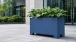 Blauer Apollo 14 Pflanzkübel aus Aluminium auf Füßen, bepflanzt mit üppigen Hostas, vor einem modernen Bürogebäude