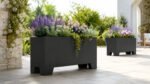 Zwei schwarze Apollo 16 Pflanzkübel aus Aluminium mit farbenfroher Bepflanzung auf einer hellen Gartenterrasse, einer im Vordergrund und einer dekorativ im Hintergrund