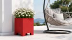 Roter Pflanzkübel Apollo 2 Mobile aus Aluminium mit weißen Margeriten auf einer hellen Terrasse neben einer Hängeschaukel