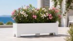 Weißer Apollo 22 Pflanzkübel aus Aluminium mit rosa und weiß blühendem Oleander auf einer hellen Terrasse mit mediterranem Ausblick