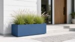 Blauer Pflanzkübel aus Aluminium mit blühendem Ziergras vor einem modernen Haus am Eingangsbereich mit hellen Stufen und klarer Architektur