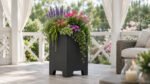 Schwarzer Pflanzkübel Apollo 3 aus Aluminium mit farbenfrohen Blüten und grünen Pflanzen in einer hellen Gartenlaube