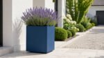 Blauer Pflanzkübel Apollo 3 Mobile aus Aluminium mit Lavendel auf hellem Pflaster neben einer Garteneinfahrt