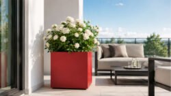 Roter Pflanzkübel Apollo 9 Mobile aus Aluminium mit weißen Rosen auf einem hellen Balkon neben modernen Gartenmöbeln