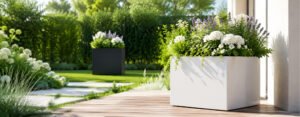 Fiberglas Pflanzkübel Marco 1 in Weiß mit blühender Bepflanzung auf einer sonnigen Terrasse und schwarzem Modell im Gartenhintergrund