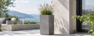 Blog 65 Grauer Beton-Pflanzkübel Davide 1 mit blühendem Ziergras auf einer hellen, modernen Terrasse