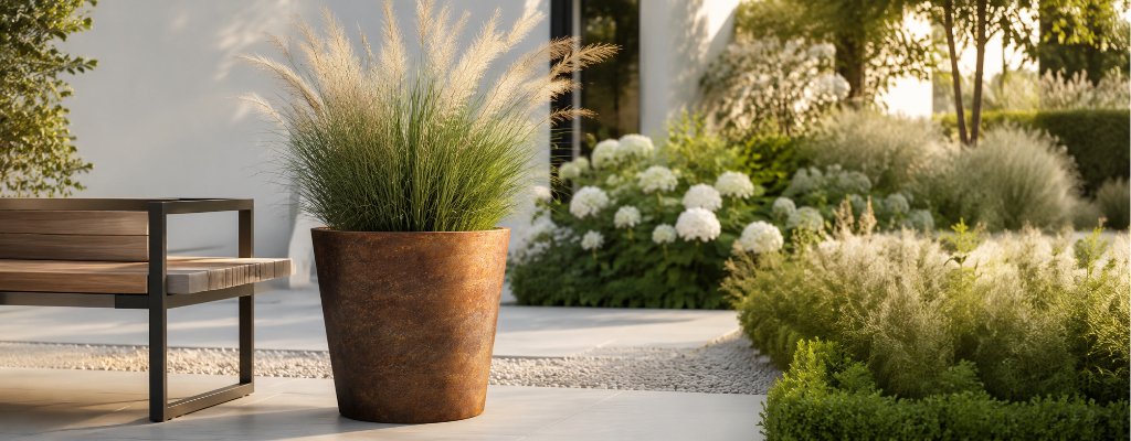 Können Cortenstahl - Pflanzkübel Rostflecken auf der Terrasse hinterlassen? 2 Vaso 6 – eleganter, konisch geformter Pflanzkübel aus Cortenstahl mit blühendem Ziergras neben einer modernen Gartenbank