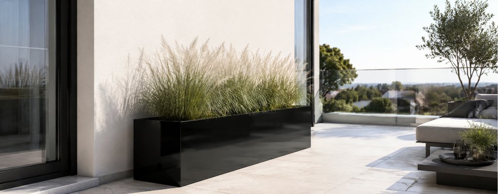 Schwarzer Aluminium-Pflanzkübel Edoardo 13 in glänzender Optik mit dekorativem Ziergras auf einem hellen, modernen Balkon