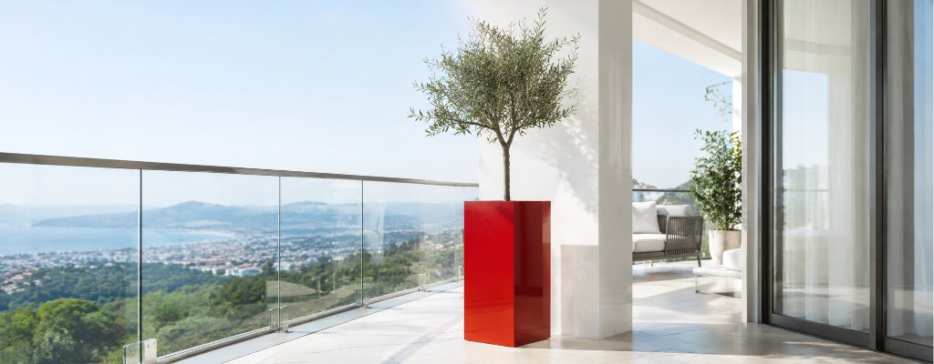 Wie winterfest sind Pflanzkübel aus Fiberglas 2 Hoher roter Pflanzkübel aus Fiberglas auf einem modernen Glasbalkon, bepflanzt mit einem eleganten Olivenbaum