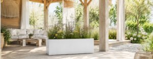 Blog 49 Bruno Pflanzkübel in weißer Betonoptik mit Wildblumen unter einer hellen Holzpergola im Garten